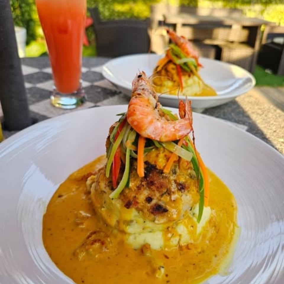 Two plates of shrimp and vegetable-topped seafood with orange sauce, and a drink on a checkered table.