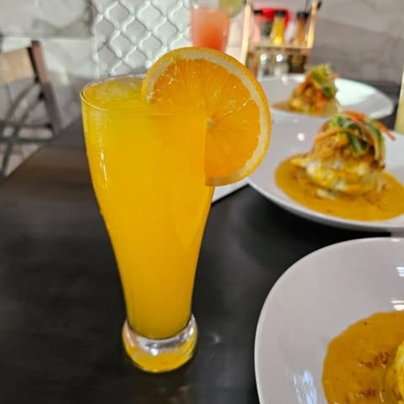 Orange juice with an orange slice garnish, and two plates of food in the background.
