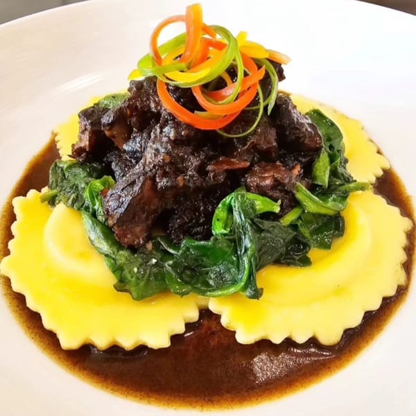 Braised short ribs with spinach and colorful bell pepper strips on ravioli in a rich sauce.