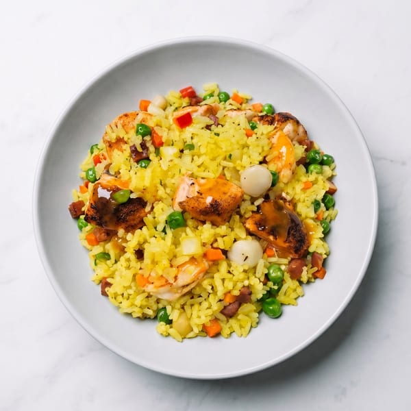 Yellow rice with shrimp, peas, carrots, and other vegetables in a white bowl.