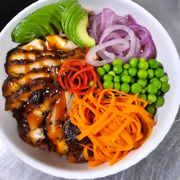 Teriyaki chicken bowl with avocado, red onions, peas, and shredded carrots in a white bowl.
