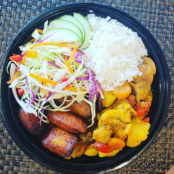 A black bowl filled with white rice, curried chicken and vegetables, fried plantains, and a fresh salad.