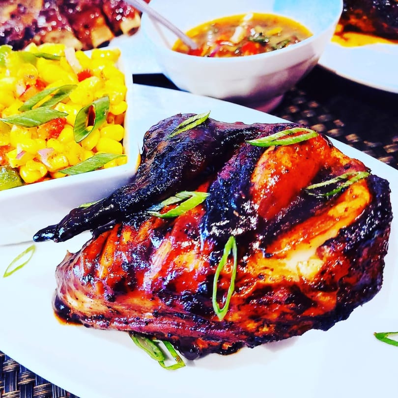 Glazed chicken with corn salsa and a bowl of soup on a white plate.