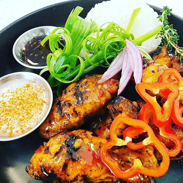 Glazed chicken wings with rice, red bell peppers, green onions, red onion, and dipping sauces.