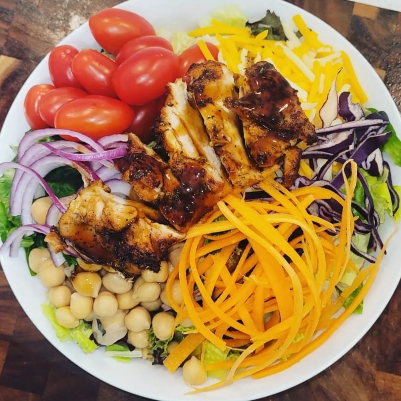 A vibrant salad with grilled chicken, cherry tomatoes, chickpeas, red onion, shredded carrots, and cheese.